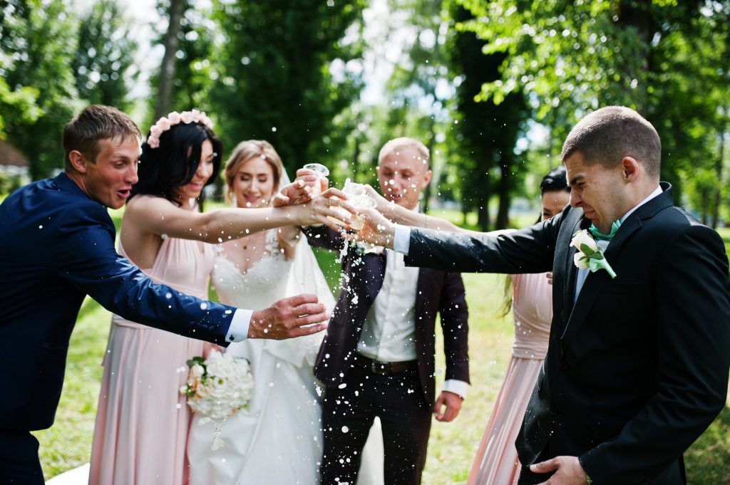 Wedding couple cheering champagne glasses with bridesmaids and best man at park.