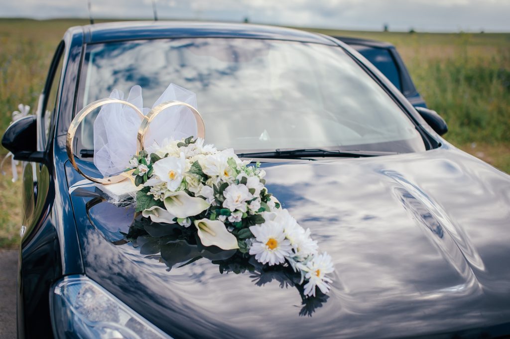 white flowers and wedding rings on the hood of the black car